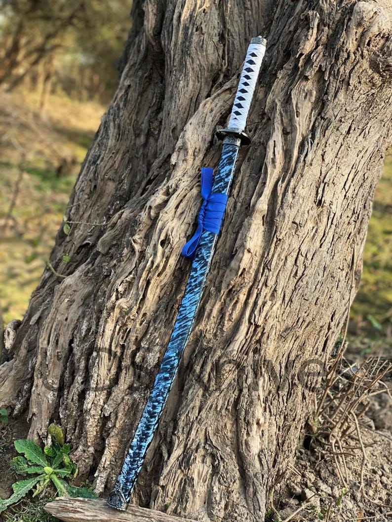 May include: A katana sword with a blue and black patterned blade and a white handle. The sword is adorned with a blue ribbon near the hilt. The blade has a textured appearance, and the handle is wrapped in white material.