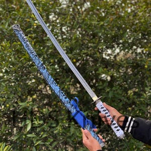 May include: A katana sword with a silver blade and white and black handle is held next to its blue patterned scabbard. The scabbard has a blue ribbon tied around it. The background is a green bush.