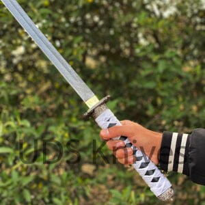 May include: A katana sword with a silver blade and a white and black wrapped handle. The handle has decorative metal accents. The text "UDS Knives" is visible on the image.