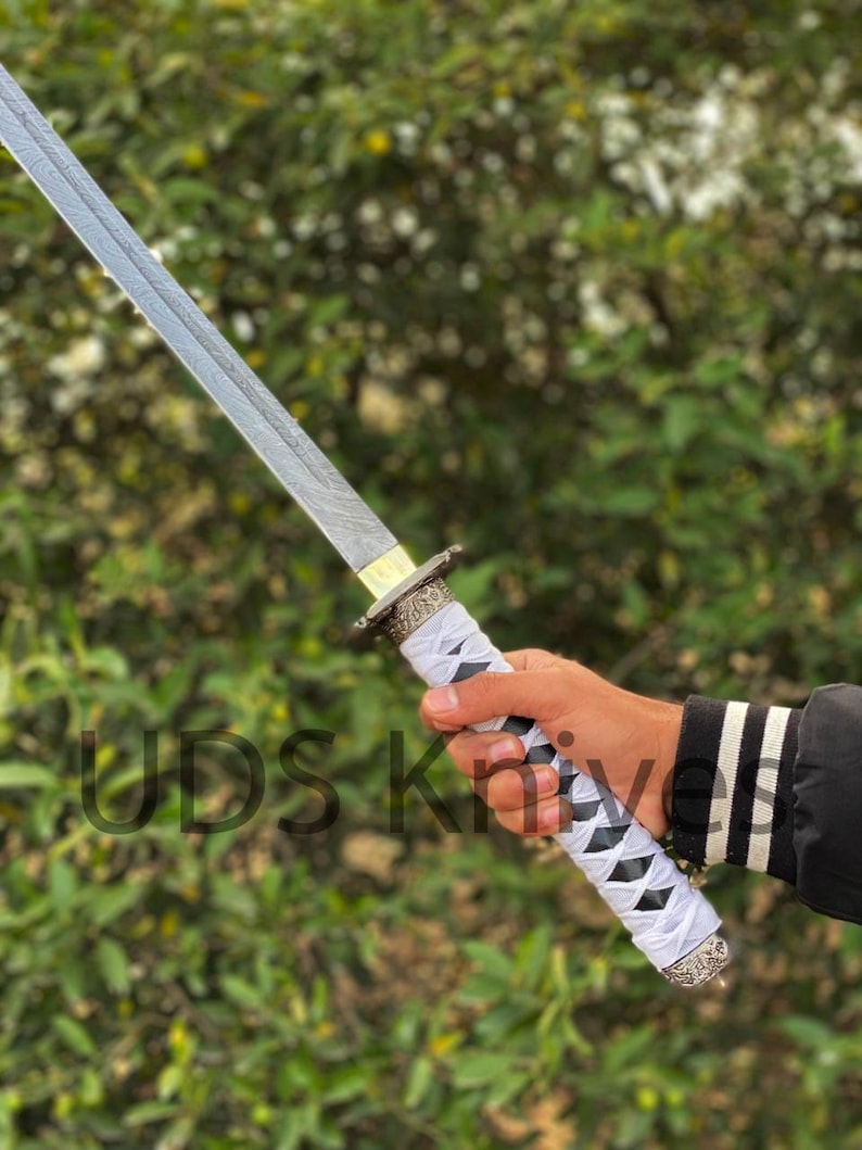 May include: A katana sword with a silver blade and a white and black wrapped handle. The handle has decorative metal accents. The text "UDS Knives" is visible on the image.