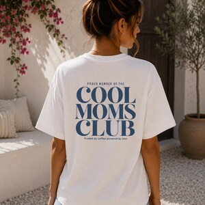 Peut inclure: Un t-shirt blanc à manches courtes avec un texte bleu foncé au dos indiquant PROUD MEMBER OF THE COOL MOMS CLUB et en dessous, Fueled by coffee powered by love. Le t-shirt est associé à un short en jean bleu clair aux bords effilochés.