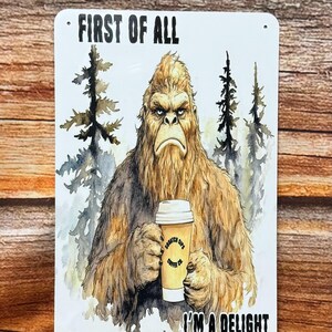 May include: A rectangular metal sign featuring a watercolor illustration of a Bigfoot holding a coffee cup. The sign reads "FIRST OF ALL" at the top and "I'M A DELIGHT" at the bottom. The coffee cup has the text "Sasquatch Sips Coffee Co."