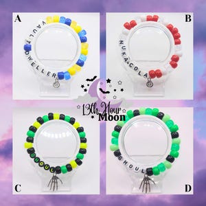 May include: Four colorful beaded bracelets with text and charms. One bracelet reads "VAULT DWELLER" in blue, yellow, and white beads. Another says "NUKA COLA" in red and white beads. The other two say "GHOUL" in green, black, and yellow beads.