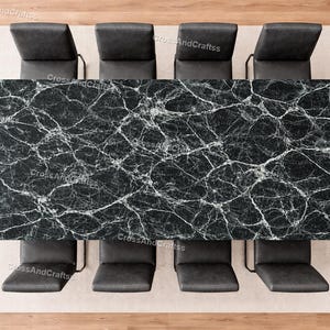 May include: An overhead shot of a dining table with a black marble top and six black leather chairs. The rectangular table has white veining. The chairs are arranged on a light beige rug.