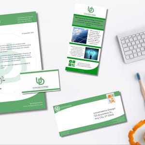 Op de afbeelding: Een briefpapier set met een groen en wit ontwerp, inclusief briefhoofd, visitekaartje en envelop. Er is ook een promotieflyer aanwezig, samen met een toetsenbord, potloden en een tandenborstel. Het briefpapier toont het logo "Universaenia Design".