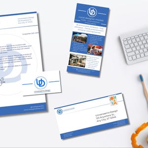 May include: A collection of stationery with a blue and white design, including a letterhead, business card, and envelope. A promotional flyer for a local designer market is also present, along with a keyboard, pencils, and a toothbrush.