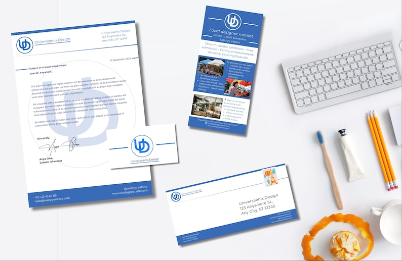 May include: A collection of stationery with a blue and white design, including a letterhead, business card, and envelope. A promotional flyer for a local designer market is also present, along with a keyboard, pencils, and a toothbrush.