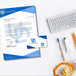 Op de afbeelding: Een zakelijke briefpapier set met een blauw en wit ontwerp, inclusief briefhoofd en visitekaartje. Het briefhoofd toont de tekst "Universaenis Design" en contactgegevens. Een toetsenbord, potloden en een tandenborstel zijn ook zichtbaar.