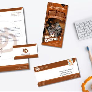 Op de afbeelding: Briefpapier set met een briefhoofd, visitekaartjes en een promotieflyer voor een bordspellenbeurs. Het ontwerp maakt gebruik van een bruin en wit kleurenschema met het "Universaenix Design" logo. Een toetsenbord, potloden en een tandenborstel zijn ook zichtbaar.