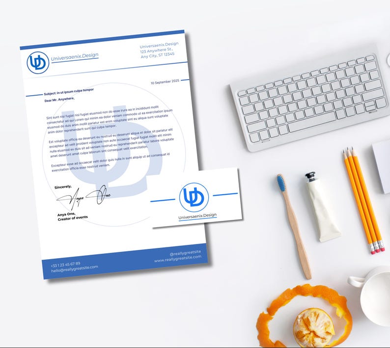 May include: A top-down view of a workspace featuring a letterhead, business card, keyboard, pencils, and a toothbrush. The letterhead and card display the "Universaenix Design" logo and contact information. A half-eaten orange sits near a white mug.