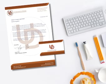 May include: A stationery set featuring a letterhead and business card with the "Universaenix Design" logo in brown and white. A keyboard, pencils, toothbrush, and a cup are also on the white surface.