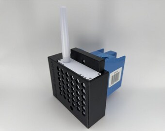 May include: A black rectangular device with a honeycomb-patterned front panel and a white top plate. A vertical white antenna extends from the top. A blue plastic component is attached to the back, featuring a white label with a barcode.