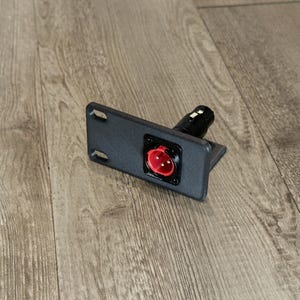 May include: A black rectangular panel mount featuring a three-pin XLR connector with a red interior insert. The mount includes two elongated mounting slots on the left side and a black cylindrical housing extending from the rear.