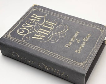 May include: A grey book with gold lettering and trim. The title "Oscar Wilde" is prominently displayed on the cover, along with the title "The picture of Dorian Gray". The book has gold corner protectors.