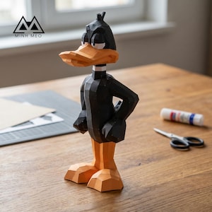 Peut inclure: Une figurine en papier low-poly représentant un canard noir au bec et aux pattes orange, debout de profil. La figurine présente des facettes géométriques nettes et un col blanc. Le texte MINH MEO est imprimé dans le coin supérieur gauche.