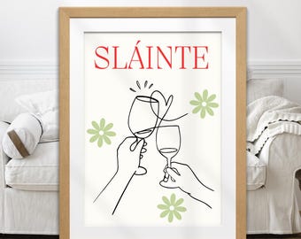 May include: A framed art print with a light wood frame. The print features the word "SLÁINTE" in red, with a line drawing of two hands toasting wine glasses. Green flower illustrations are scattered around the glasses.