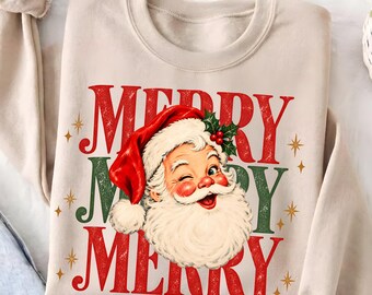 May include: A beige crewneck sweatshirt featuring a graphic of a winking Santa Claus wearing a red hat with holly. The text MERRY MERRY MERRY is printed in red and green with a distressed texture, accented by small gold star illustrations.