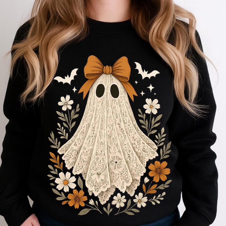 May include: Black sweatshirt featuring a Halloween ghost design. The ghost is made of white lace and has a brown bow. The design includes white bats, flowers, and stars. A festive and stylish apparel item for the spooky season.
