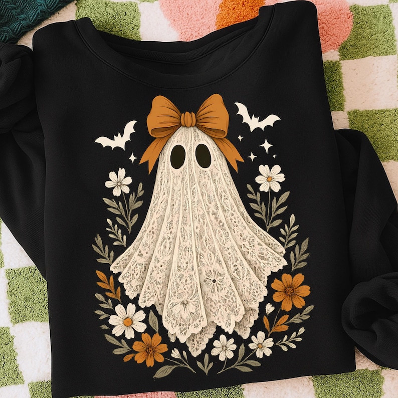 May include: Black sweatshirt featuring a ghost design. The ghost is white with a lace-like pattern, a brown bow, and surrounded by flowers and bats. A festive Halloween-themed apparel item.