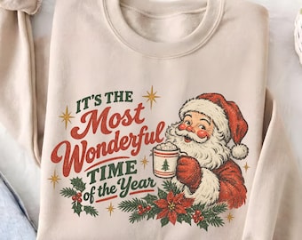 May include: A beige crewneck sweatshirt featuring a graphic of Santa Claus holding a mug with a small tree print. The text reads, "IT'S THE MOST WONDERFUL TIME OF THE YEAR," surrounded by gold star accents, green holly leaves, and red poinsettia flowers.