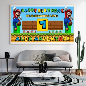 May include: A framed birthday banner featuring a Super Mario theme. The banner reads "Happy Birthday, He is Reaching Level 7, Alex Adventure" with Mario characters and game elements. The banner is displayed above a gray sofa.
