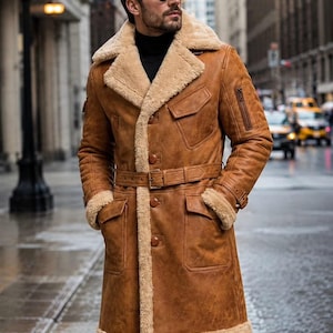 Puede incluir: Una gabardina de cuero color canela con un grueso forro de borrego beige, cuello ancho con muescas y cinturón en la cintura. El abrigo incluye dos grandes bolsillos delanteros con solapa, un bolsillo utilitario con cremallera y botones marrones.