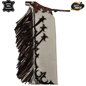 Puede incluir: Chaps de cuero blanco con flecos marrones y detalles decorativos. Los chaps presentan un cinturón de cuero marrón y adornos en forma de estrella. La parte superior tiene un diseño floral. La imagen incluye un logotipo "Genuine 100% Leather".