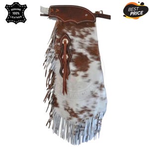 May include: Cowhide leather chaps with a brown and white spotted pattern. The chaps feature a brown leather yoke, decorative stitching, and fringe along the sides. The image includes a "Genuine 100% Leather" logo.
