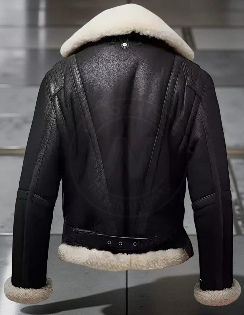 May include: Black leather jacket with a cream-colored shearling collar and trim. The jacket features a belted waist, a zipper closure, and a classic aviator style. The back of the jacket has a distinctive V-shaped design.