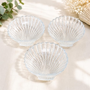 May include: Three clear glass dishes shaped like scallop shells. Each dish features a series of raised, radiating ridges that extend from the base to the scalloped edge, creating a textured, fan-like appearance with a translucent finish.