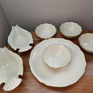 May include: A cream-colored porcelain serving set featuring leaf-shaped dishes and bowls with gold trim. The set includes a large platter, a small bowl, and several smaller bowls, perfect for serving appetizers or desserts.