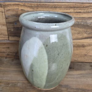 May include: A handmade ceramic vase with a rounded body and a slightly flared rim. The vase features a blend of green, white, and gray tones, with a crackled texture. The pottery is suitable for home decor.
