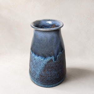 May include: A ceramic vase with a wide, rounded rim and a tapered neck that widens toward the base. The exterior features a reactive glaze with deep navy blue and dark brown tones, showing a mottled texture and a smooth, glossy finish throughout.