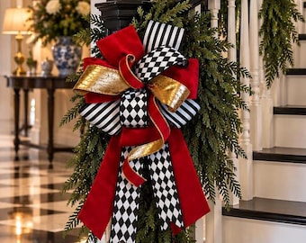 May include: A decorative bow attached to a green evergreen garland on a staircase banister. The bow features a combination of solid red velvet ribbon, gold metallic ribbon, black and white striped ribbon, and black and white diamond patterned ribbon.