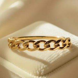 Pode incluir: Um anel de corrente dourada. O anel é feito de ouro e apresenta um design contínuo de elos de corrente. O anel é exibido em uma superfície de veludo branco.