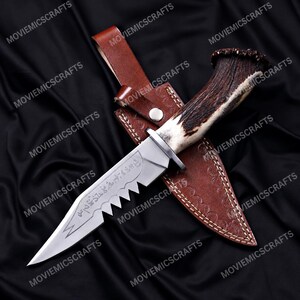 May include: A fixed-blade knife with a serrated spine and etched markings on the silver-toned steel blade. The handle is crafted from textured brown antler, and the knife is accompanied by a brown leather sheath featuring a snap button closure.