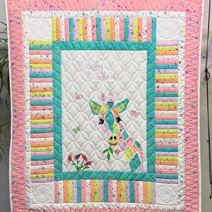 May include: A baby quilt with a giraffe design. The quilt features a white center with a giraffe applique, surrounded by a teal border and colorful striped sections. The outer border is pink with a floral pattern.