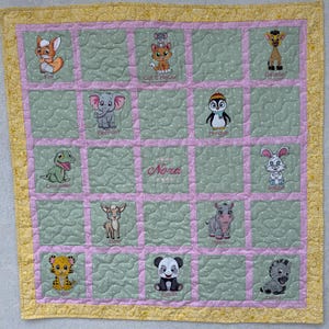 May include: A handmade baby quilt with embroidered animal designs, including a fox, cat, elephant, penguin, giraffe, rabbit, crocodile, deer, hippo, tiger, panda, and zebra. The quilt features a pink and green color scheme with the name "Nora" embroidered in the center.