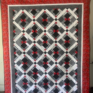 May include: A black, white, and red quilt with a diamond pattern. The quilt is made of different fabrics with various patterns, including polka dots, stripes, and animal prints.