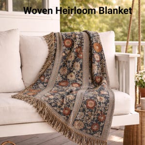 Könnte beinhalten: Gewebte Erbstück-Decke mit floralem Muster in Marine-, Braun- und Beigetönen. Die Decke hat einen Fransenrand und ist über einer weißen Gartenbank drapiert. Der Text "Woven Heirloom Blanket" steht oben.