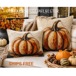 May include: Two square scatter cushions featuring an oil painting style print of orange and brown pumpkins with textured brushstrokes on a cream background. The cushions are displayed on a white outdoor sofa with a woven basket of small pumpkins.