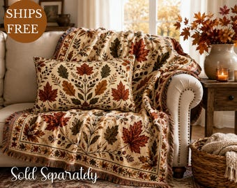 May include: A rectangular throw pillow and a matching woven throw blanket, both featuring a cream-colored background with a repeating pattern of autumn leaves in shades of orange, red, and dark green, accented with small brown berries.