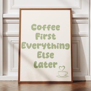 May include: A rectangular wall art print in a wooden frame featuring the sage green text Coffee First Everything Else Later on a cream background. Below the text is a simple line drawing of a coffee cup with a heart-shaped steam rising above it.