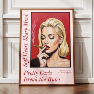 Peut inclure: Une affiche murale rectangulaire encadrée représentant une personne blonde aux lèvres rouges tenant une cigarette allumée avec de la fumée. Le texte indique : Soft Heart. Sharp Mind. Pretty Girls Break the Rules. A Little Sweet. A Little Dangerous.