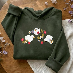 May include: Dark green hoodie with a hood and long sleeves. The front features an embroidered design of three white birds with strawberries and flowers. The hoodie is made of a soft material and is suitable for casual wear.