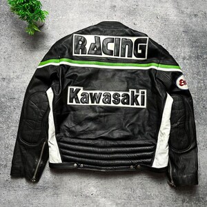 May include: Black leather racing jacket with white and green accents. The back features the word "RACING" across the shoulders and "Kawasaki" below. The jacket has a quilted design on the lower back and white panels on the sides.