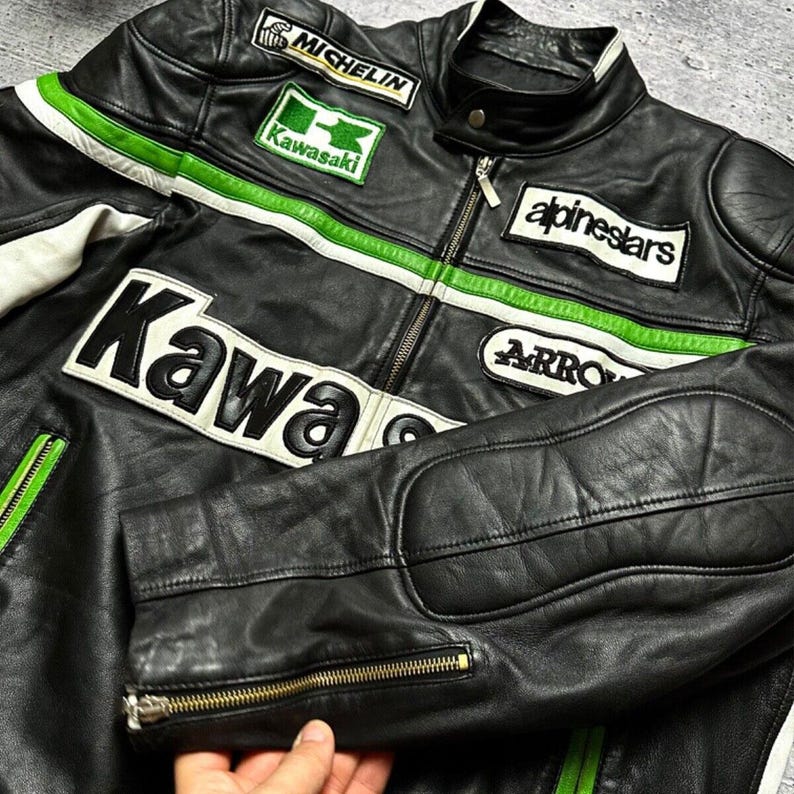 May include: Black leather motorcycle jacket with green and white accents. Features embroidered patches including "Kawasaki", "Michelin", and "Alpinestars". Includes a zippered front closure and zippered sleeve cuffs. The jacket has padded elbow patches.