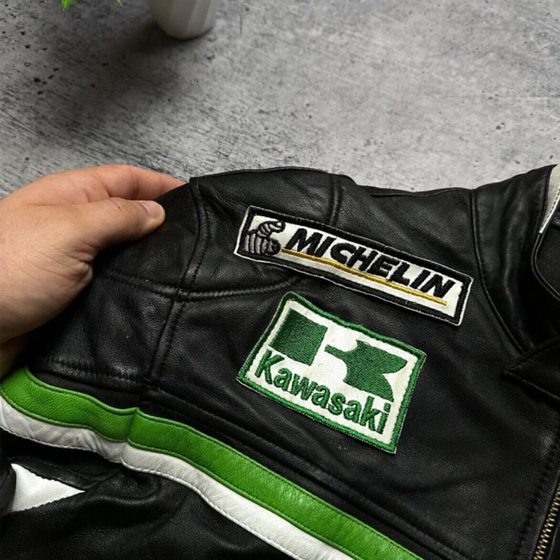 May include: Black leather motorcycle jacket with green and white accents. Features "Michelin" and "Kawasaki" patches. The jacket has a zipper closure and a classic design.