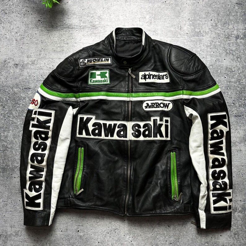 May include: Black leather motorcycle jacket with white and green accents. Features the Kawasaki logo and text, along with patches from Michelin, Alpinestars, and Arrow. The jacket has a zippered front and white detailing on the sleeves.