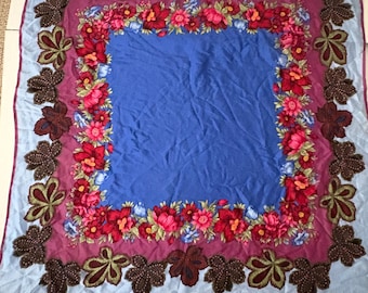 Könnte beinhalten: Ein quadratischer Schal mit blauem Zentrum, umrahmt von einem floralen Rand aus roten und rosa Blumen auf violettem Hintergrund. Der äußere Rand weist braune blattartige Designs auf, alles vor einem hellblauen Hintergrund.